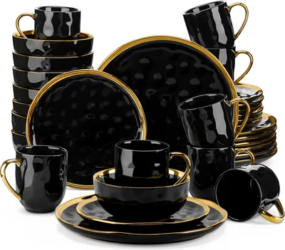 A collection of black ceramic dinnerware with gold trim, including plates, bowls, and cups, arranged in stacks.