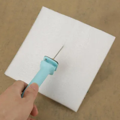 A hand holding a foam cutter to cut a piece of white foam.