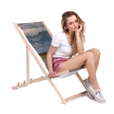 A woman sitting on a beach chair with a mountain landscape printed on it.