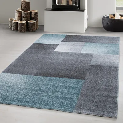 A modern abstract rug with geometric patterns in shades of gray and blue, placed on a light gray floor.