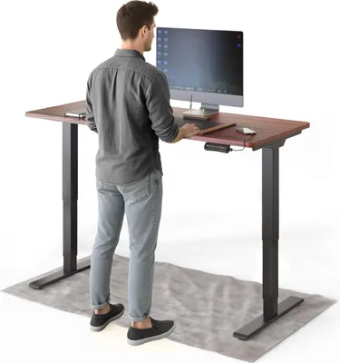 A man stands at a standing desk, working on a computer.