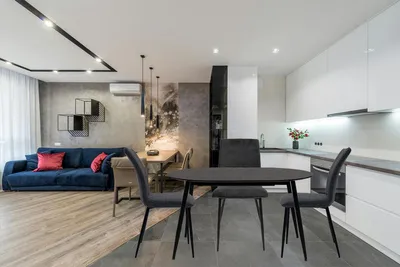 A modern open-plan living and dining area with a blue sofa, dining table and chairs, and a white kitchen.