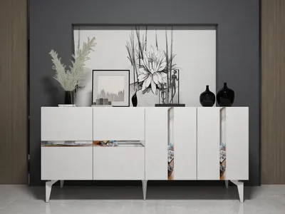 A white console table with decorative elements on top and on the doors, set against a dark gray wall and a white floor.