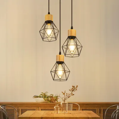 Three pendant lights with geometric metal cages and wooden accents hang above a wooden table with decorative items.