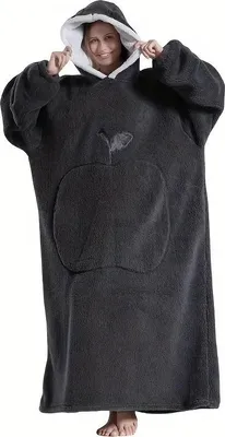 A woman wearing a dark gray oversized hoodie blanket with a white interior lining and a pocket with an apple design.