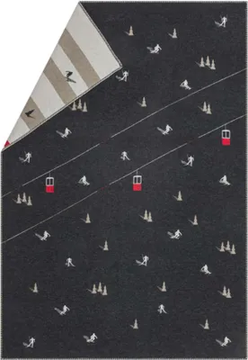 A folded blanket with a ski slope pattern on a dark gray background. The blanket is folded to reveal a striped pattern on the underside.