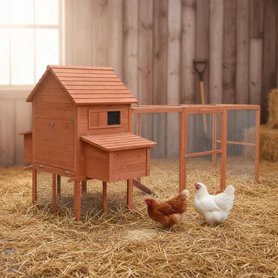 A wooden chicken coop with an attached run, set in a straw-covered outdoor area with hay bales and a shovel in the background.