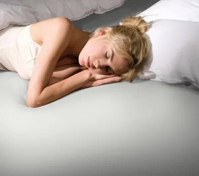A woman sleeping peacefully on a bed with white bedding.
