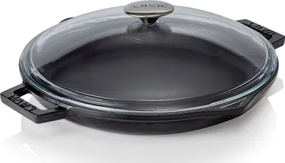 A black cast iron pan with a clear glass lid and silver handle, shown from a slightly elevated angle on a white background.