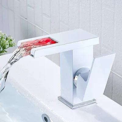 A modern white waterfall faucet with red LED lighting is shown in use over a white sink.