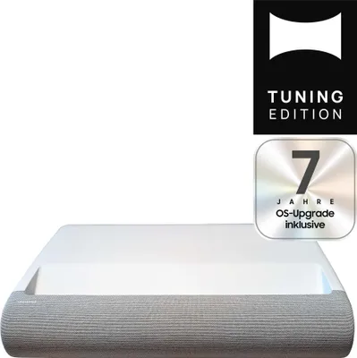 A white DLP projector with a gray fabric front, placed on a white background. There are two marketing badges in the top right corner.