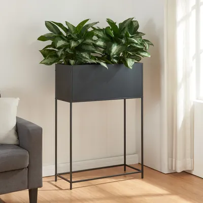 A black metal planter stand with green plants on a wooden floor next to a gray sofa and a white curtain.