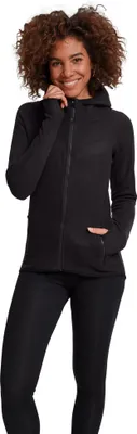 A woman wearing a black zip-up hoodie and black leggings, posing against a white background.