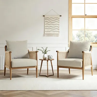 Two beige rattan chairs with comfortable cushions are placed in a well-lit room with a window and a small wooden table between them.