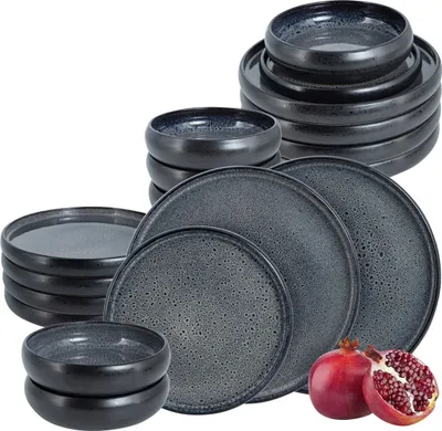 A collection of dark gray ceramic plates and bowls are stacked and arranged on a white background. Two pomegranates are placed in the foreground.