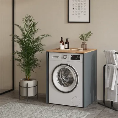 A washing machine cabinet with a wooden top, placed in a bathroom setting with a plant and towels.