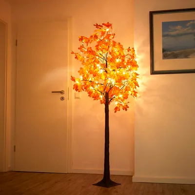 An LED tree with orange leaves and warm white lights stands in a hallway next to a door and a framed picture.