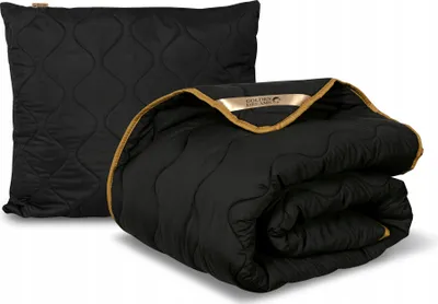 A black quilted pillow and a folded black quilted blanket with gold trim are displayed against a white background.