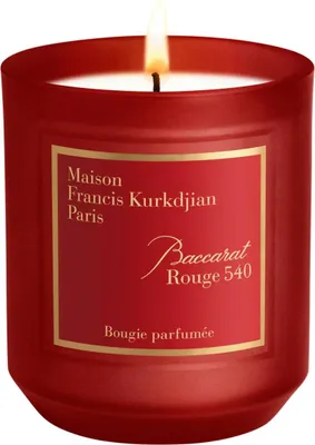 A lit scented candle in a red glass jar with a gold label.