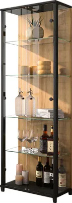 A tall, narrow glass display cabinet with a black frame and wood-effect back panel, filled with various items like bottles, glasses, and decorative objects.