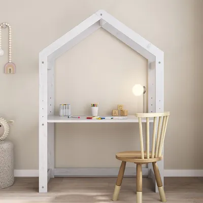 A child's desk shaped like a house, with art supplies and a lamp on the desk, and a chair next to it.