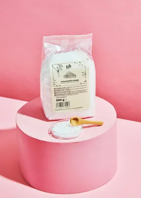 A bag of pyramid salt sits on a pink pedestal, with a small dish of salt and a wooden spoon in front of it.