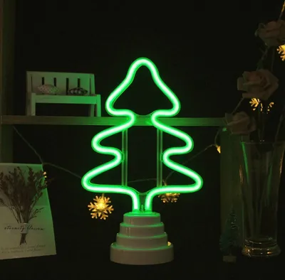 A green neon Christmas tree light on a white base, displayed on a shelf with other decorative items.