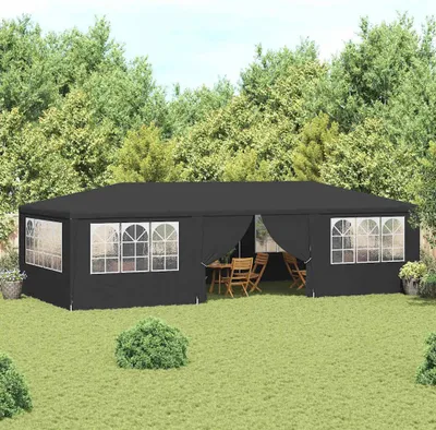 A black party tent set up in a grassy backyard with trees in the background.