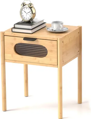 A wooden nightstand with a drawer and a glass insert, shown with a clock, books, and a cup of coffee on top.