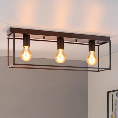 A black metal ceiling light fixture with three exposed Edison-style bulbs is shown against a white ceiling and gray wall.