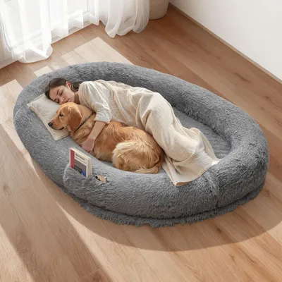 A woman and a dog are sleeping together on a large, plush dog bed.