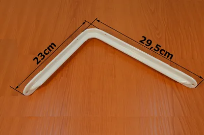 A white L-shaped bracket is placed on a wooden surface, with measurements indicated.