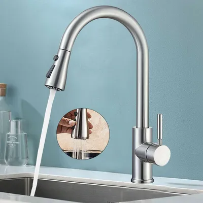 A stainless steel kitchen faucet with a pull-down sprayer is shown in use over a sink.