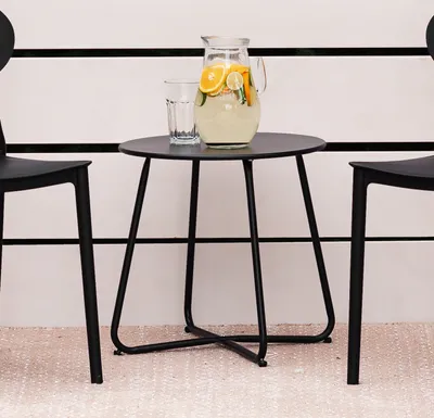 A black metal side table with a pitcher of lemonade and a glass on it, placed between two black chairs.