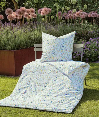 A floral patterned duvet and pillow are displayed on a chair in a garden setting.
