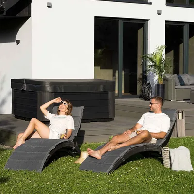 A couple relaxing on lounge chairs in a backyard next to a hot tub.
