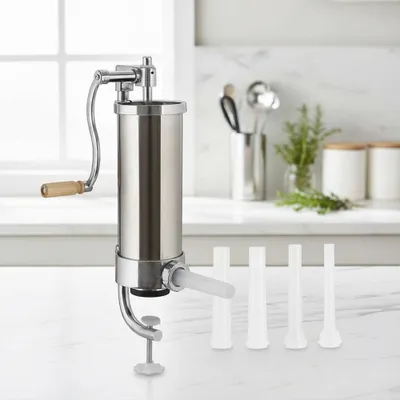 A stainless steel vertical sausage stuffer with a hand crank and four filling funnels sits on a marble countertop in a kitchen setting.