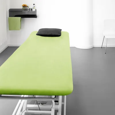 A clean, well-lit room with a massage table covered in a green sheet and a black pillow.