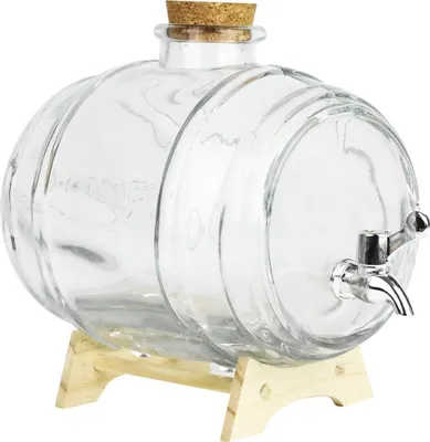 A clear glass barrel-shaped beverage dispenser with a cork stopper and a silver spigot, resting on a light wood stand.