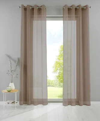 Two sheer taupe curtains hang in front of a window with a view of trees and grass. A small round table with a vase and a book sits to the left.
