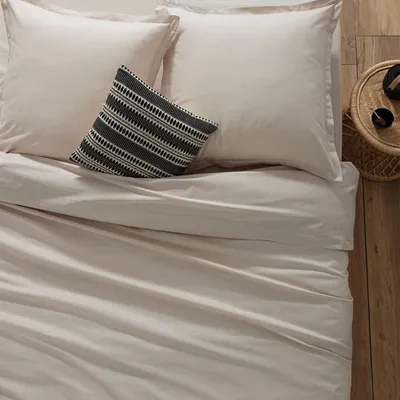 A neatly made bed with light beige bedding and a decorative pillow.