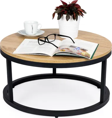 A round coffee table with a wood-look top and black metal legs, featuring a book, glasses, a cup of coffee, and a potted plant.