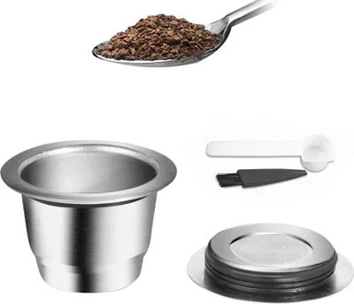 A collection of items related to coffee capsule preparation, including coffee grounds, a reusable coffee capsule, and accessories like a scoop and brush.