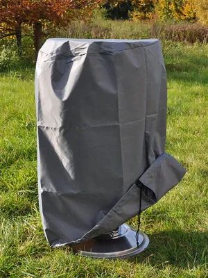 A gray cover for a grill is shown in a grassy outdoor setting.