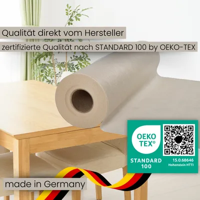 A roll of fabric is placed on a wooden table, with curtains and plants in the background.