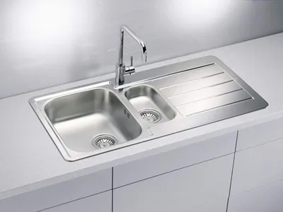 A stainless steel kitchen sink with a faucet and a draining board, installed on a white countertop.