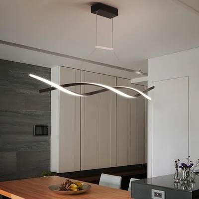 A modern dining room with a sleek, wavy pendant light fixture hanging above a wooden table.