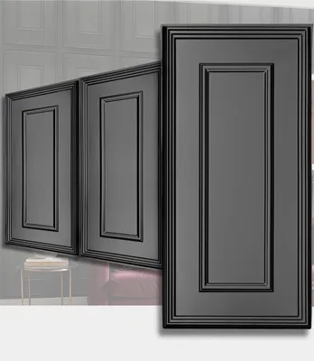 Three dark gray decorative wall panels with a raised frame design, arranged diagonally. The background shows a gray textured wall and a hint of furniture. The foreground is a white surface.