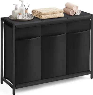 A black laundry sorter with three compartments sits on a white background. The top surface displays a tray with toiletries and folded towels.