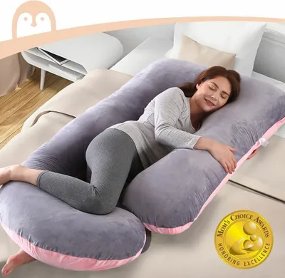 A pregnant woman is sleeping comfortably on a large U-shaped pillow in a bedroom.